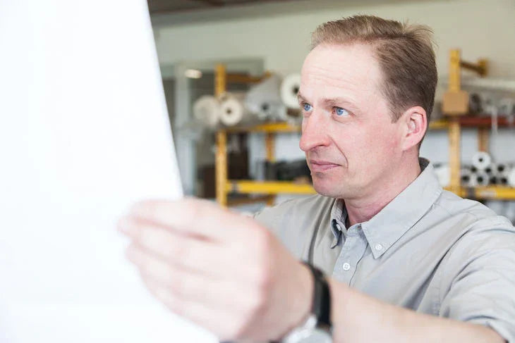 Mitarbeiter prüft technische Zeichnung im Industriefilter-Lager, Regale mit Filtermaterial im Hintergrund Mitarbeiter prüft technische Zeichnung im Industriefilter-Lager, Regale mit Filtermaterial im Hintergrund