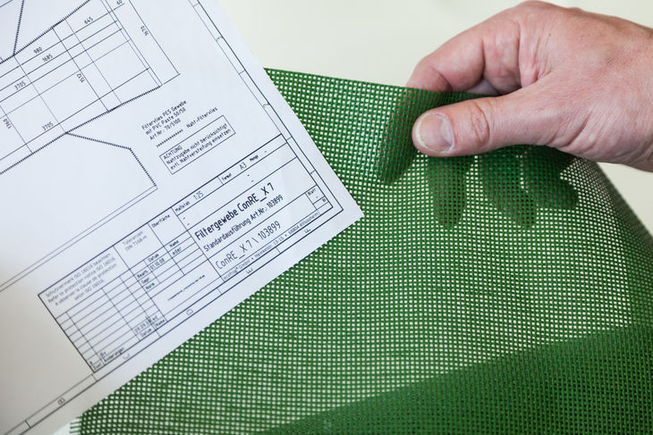 Hand hält grünes Filtergewebe und technische Zeichnung für Industriefilter Hand hält grünes Filtergewebe und technische Zeichnung für Industriefilter
