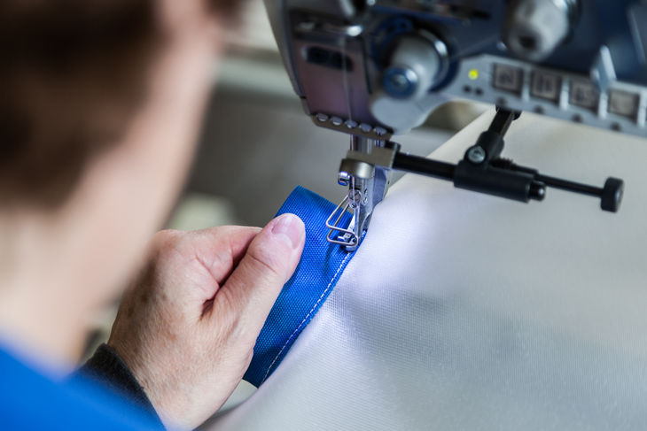 Nahaufnahme Industrienähmaschine näht blauen Stoff, Hand richtet Material aus Nahaufnahme Industrienähmaschine näht blauen Stoff, Hand richtet Material aus