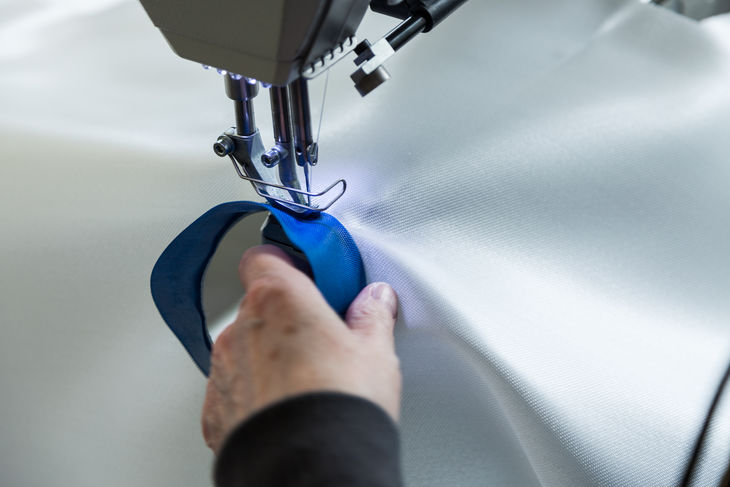 Nähen von Industriefiltergewebe mit Industrienähmaschine, Hand führt blauen Stoffstreifen Nähen von Industriefiltergewebe mit Industrienähmaschine, Hand führt blauen Stoffstreifen