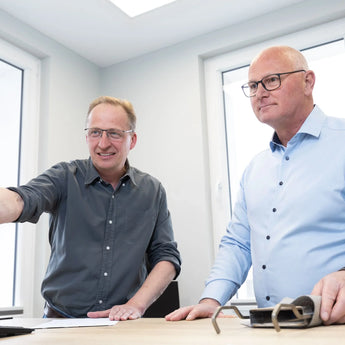 Beratung Filtertechnik Fachliche Beratung zwei Personen stehen am Tisch mit Papieren und Metallbauteil im Büro Beratung Filtertechnik Fachliche Beratung zwei Personen stehen am Tisch mit Papieren und Metallbauteil im Büro